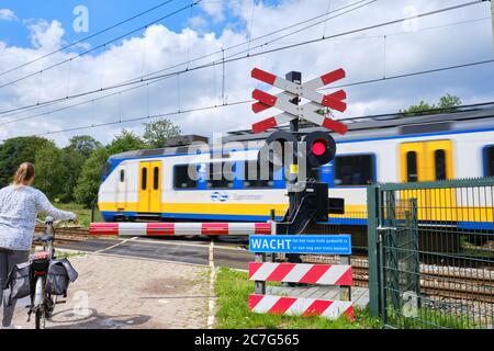 Railway crossing with barriers and blinking red lights and unsharp high speed train. Dutch text,Wait till red light is gone,possibility of other train Stock Photo