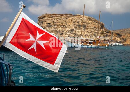 The merchant flag of Malta mounted on yacht stern waving on wind, closeup photo with selective focus and blurry sailing ship on a background Stock Photo