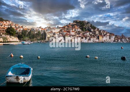 Old town of Sibenik, Croatia seen from a distant beach. Small old blue ship anchored. Mediterranean typical traditional seascape view Stock Photo