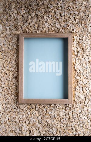 Background with natural dry rolled oats and with square copy space in wooden picture frame and with blue paper texture in it. Source of vegetable prot Stock Photo