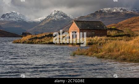 Boat house at Loch Arklet with gathering storm clouds over the Arrochar Alps, near Stronachlachar, Loch Lomond & The Trossachs National Park, Scotland Stock Photo