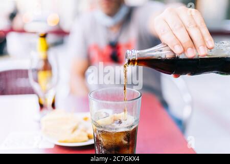 A man with a mask pours a cola drink in a glass Stock Photo