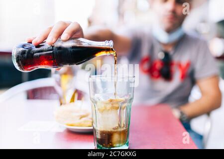 A man with a mask pours a cola drink in a glass Stock Photo