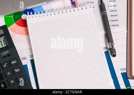 Empty Notepad page, a calculator, a pen, and financial papers with numbers on the desktop. Trade, investment, and banking. Stock Photo