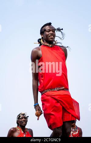 Maasai man smiling wearing traditional attire, taking part in the traditional Adumu dance, or Jumping Dance, in Maasai Mara National Reserve. Kenya. Stock Photo