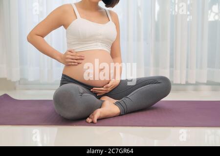 pregnancy, people and maternity concept - happy pregnant asian woman applying stretch mark cream to belly Stock Photo