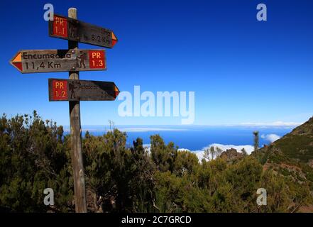 Three signs indicate hiking trails on the slopes of Pico Ruivo (Madeira, Portugal). In the background, the ocean and the blue sky merge. Stock Photo