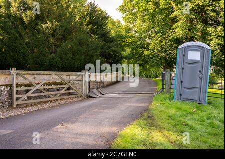 A plastic portable toilet next to a covered cattle grid on a public footpath in a field at an outdoor event. Stock Photo