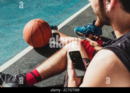young man rests after the basketball game and uses his smartphone with his friend Stock Photo