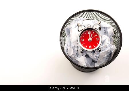 Procrastination is the enemy of productivity and stop wasting time concept theme with a clock in a black waste basket or rubbish bin next to crumpled Stock Photo
