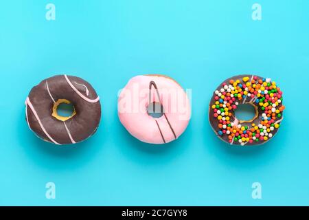Classic chocolate, pink strawberry, decorated with colorful sprinkles donut isolated on blue background Flat lay Top View Knolling Unhealthy and tasty Stock Photo
