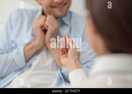 Females hand holding engagement ring proposing. Woman doing marriage proposal to her boyfriend and holding thin silver ring in her hand. Man blurred Stock Photo