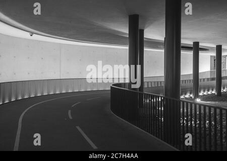 Greyscale of a tunnel surrounded by fences and columns under the lamp lights Stock Photo