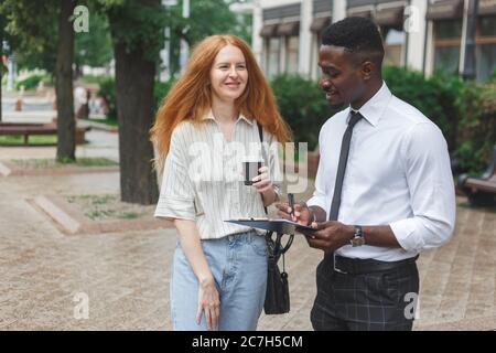 Black african american man on the street making a survey to red haired woman Stock Photo