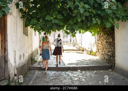 Alley with people walking through it surrounded by old buildings and greenery under sunlight Stock Photo