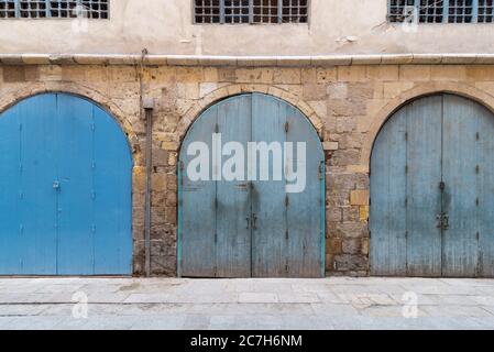 Row of closed three blue weathered wooden arched doors in stone bricks wall, located in old abandoned district Stock Photo