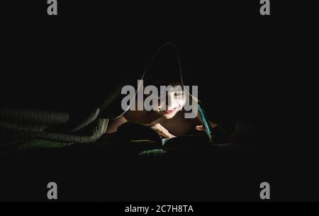 Young boy reading a book under a blanket using a flashlight. Stock Photo