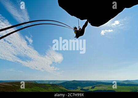 woman rappelling from cliff at Windgather rocks in the Peak District Stock Photo