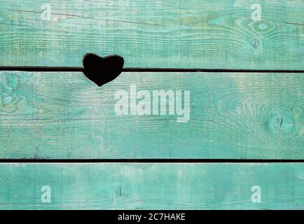 a hole in the shape of a heart in a wooden wall made of old boards painted blue Stock Photo