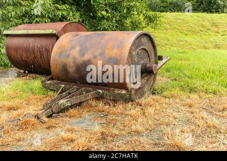 Soil roller for the handling and laying of the lawn. Old rusty metal lawn roller on some dry grass. Vintage roller for sports grounds football athleti Stock Photo