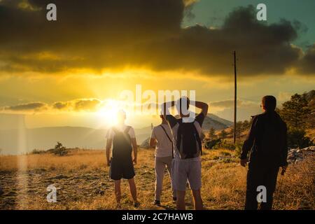 Four friends seen from behind, hiking on top of the Mosor mountain in Croatia. Strong colorful sun setting seen going behind the hill while people wat Stock Photo