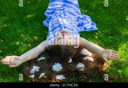 happy little girl, pretty little girl lying on grass with flowers Stock Photo