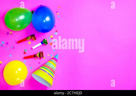 Carnival hats and accessories for birthday celebration lie on bright pink background. Scattered confetti. Copy space for text. Top view. Flat lay. Lay Stock Photo