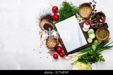 Open blank recipe book with healthy vegan ingredients for cooking and chopping board top view. Stock Photo