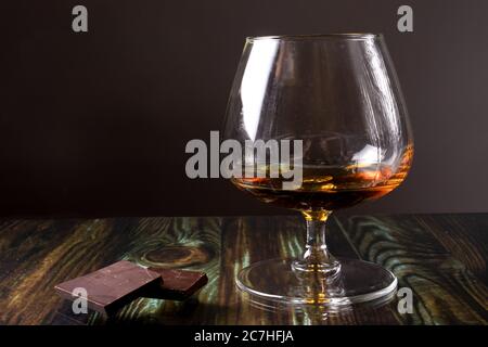 Glass with cognac and dark chocolate. Dear elite alcohol on a dark brown background. Alcoholic drinks. Stock Photo