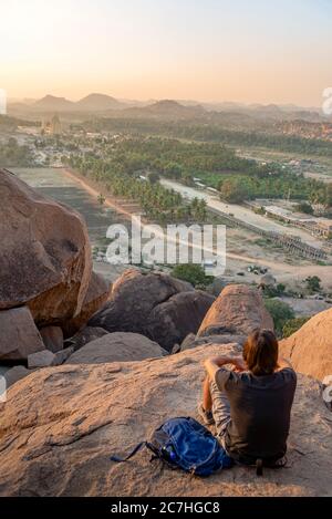Watcher sitting on the rock looks at valley at dusk Stock Photo