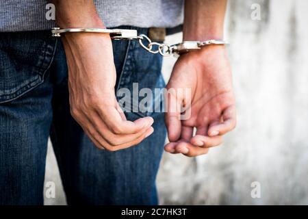 Close up hands tied up handcuffs in behind his body. Arrested man handcuffed hands at the back. Stock Photo
