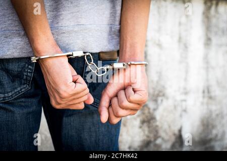 Close up hands tied up handcuffs in behind his body. Arrested man handcuffed hands at the back. Stock Photo