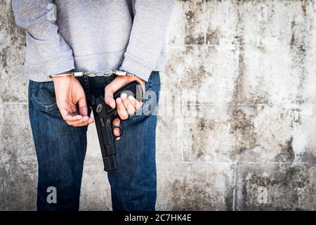 Close up hands tied up handcuffs and holding gun in behind his body. Arrested man handcuffed hands at the back. Stock Photo
