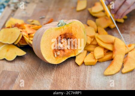 Half a Hokkaido pumpkin and pumpkin wedges, split on a wooden board with a chef's knife Stock Photo