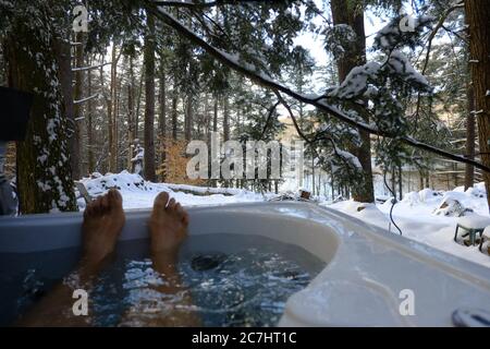 Man's feet sticking out of outdoor hot tub during winter Stock Photo