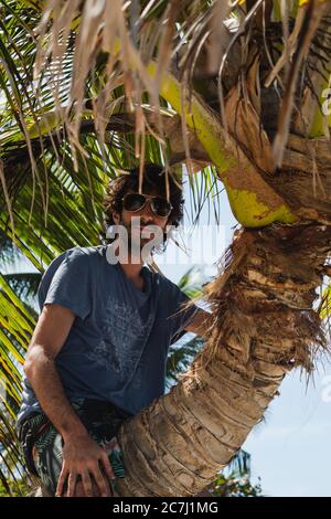 A young man sitting on the trunk of a palm tree on the beach in Culebra, Puerto Rico Stock Photo