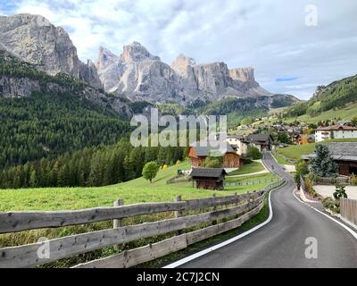 View from a slightly elevated point of view of the Dolomites and the village of Kolfuschg, with an empty road that leads into the picture Stock Photo