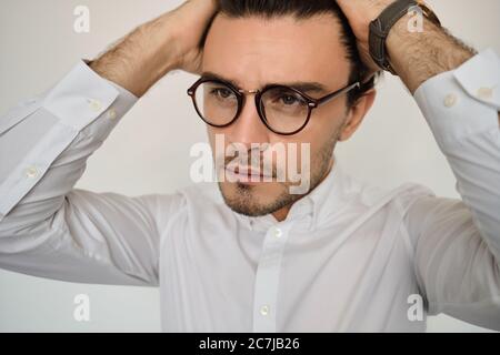 Portrait of young handsome brunette man in white shirt and eyeglasses thoughtfully looking aside over white background Stock Photo