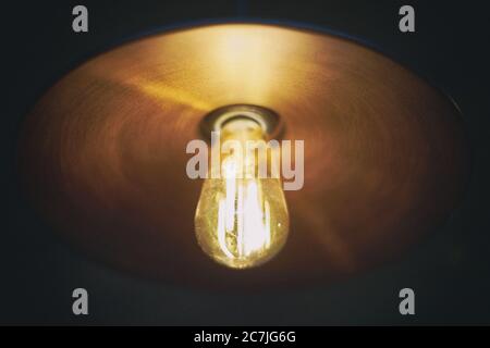 Turned-on light bulb hanging in a dark room Stock Photo