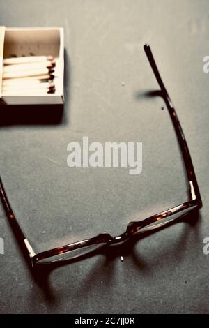Vertical high angle shot of a glasses next to a matchbox on a grey surface Stock Photo