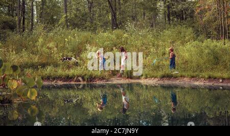 Group of kids walking through a field covered in greenery and reflecting on the lake under sunlight Stock Photo