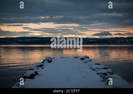 Dock covered with snow near the sea with the reflection of the sunset Stock Photo