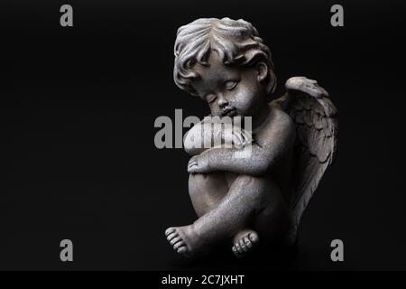 Angel figure sleeping, sitting, black background, Stock Photo