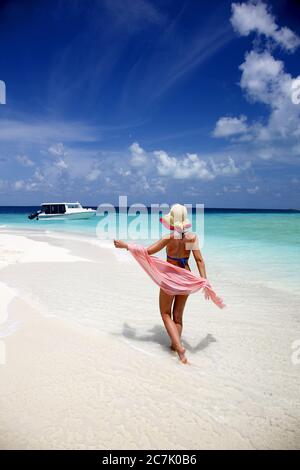 Young woman walking along deserted white sand beach surrounded by tropical waters in Maldives Stock Photo