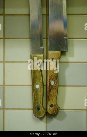 Vertical shot of knives hanged on the wall with white tiles Stock Photo