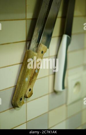 Vertical shot of knives hanged on the wall with white tiles Stock Photo