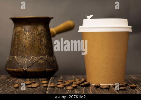 Coffee in a cardboard cup stands on a wooden table, surrounded by roasted coffee beans and coffee maker Stock Photo