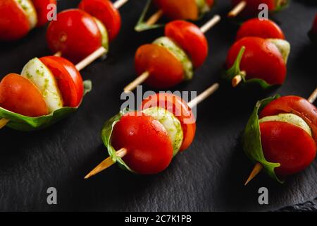 Small snacks canape with cherry tomatoes, mozzarella on skewer on a black slate plate. Stock Photo