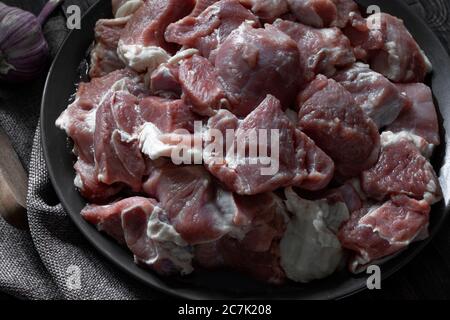 Raw mutton cut into medium pieces, lay on a plate, surrounded by garlic, burlap napkin, and a knife Stock Photo