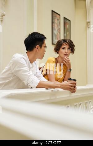 Two young international students thoughtfully talking at break in corridor of university Stock Photo